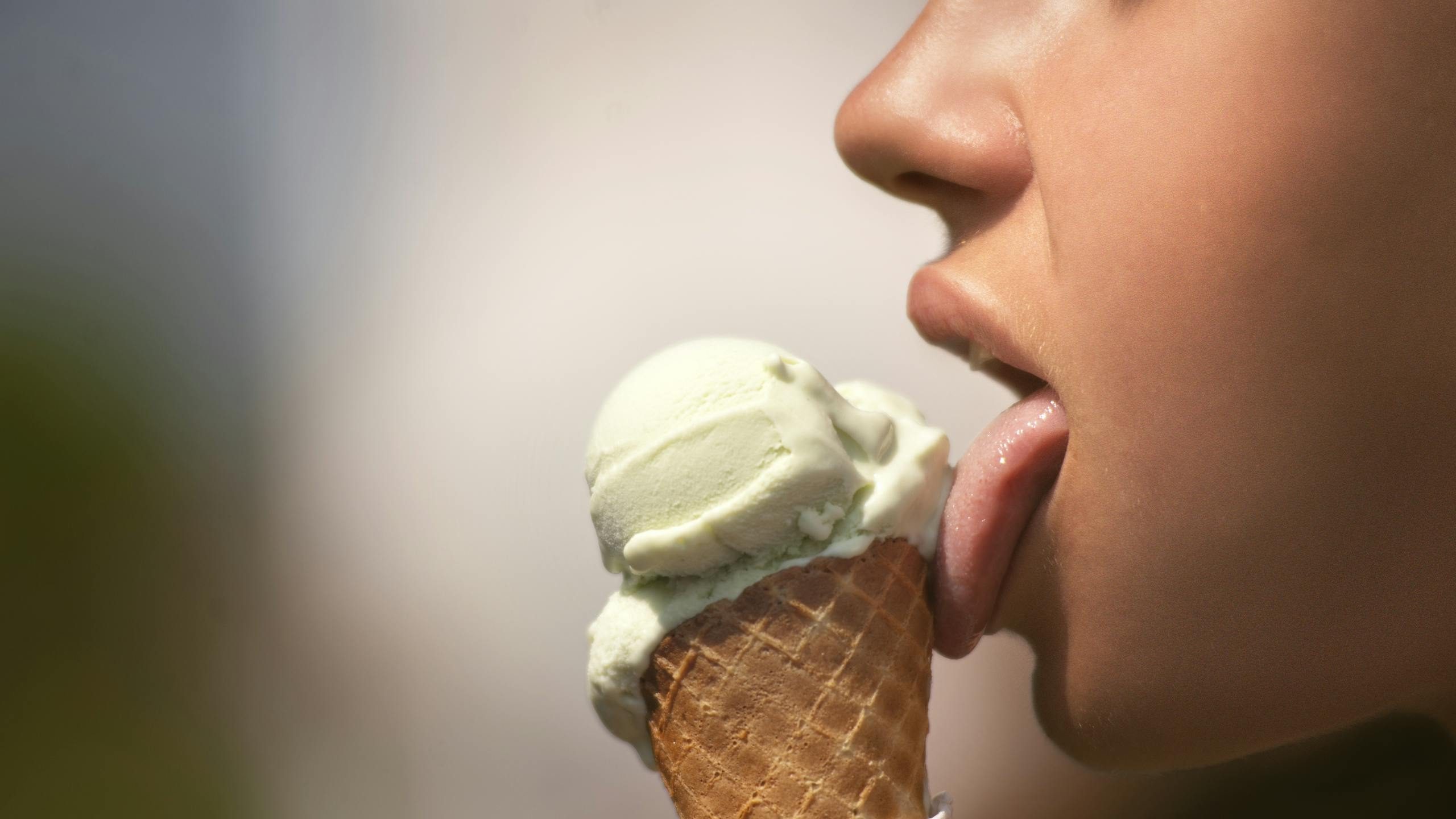 A close-up of a person enjoying a green ice cream cone on a sunny day.