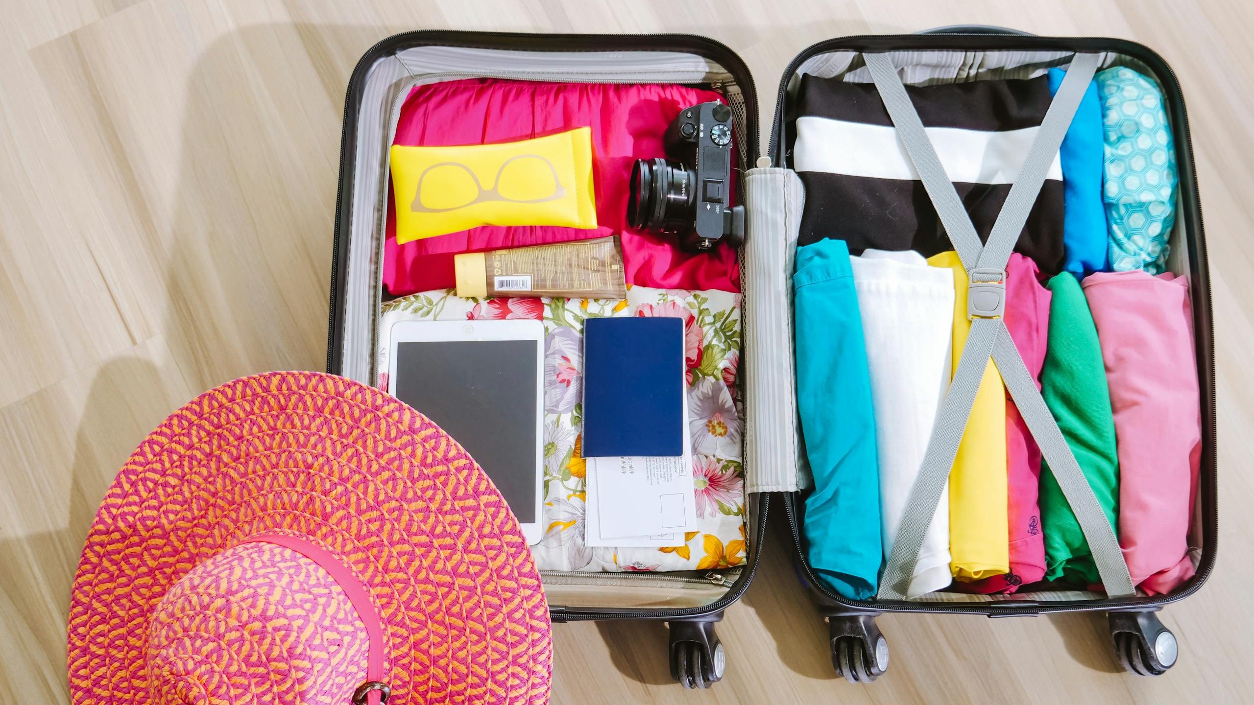 Top view of a suitcase packed with clothes, a camera, and a sun hat, ready for summer travel.